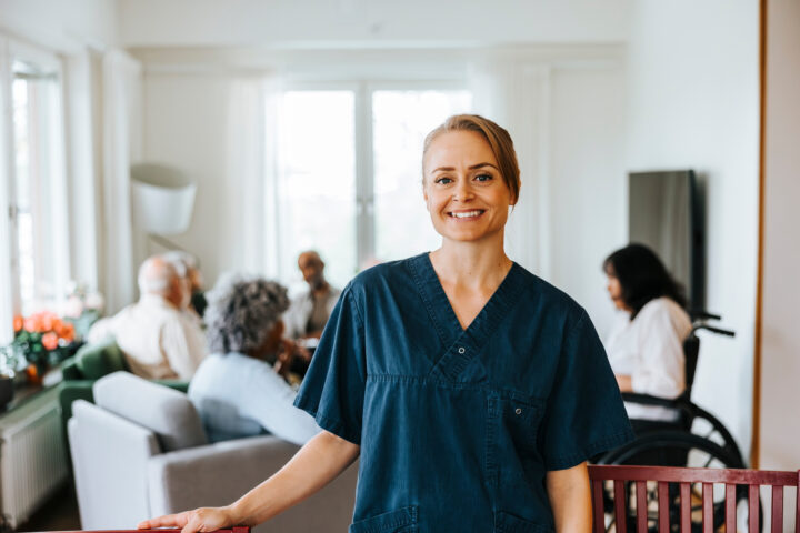 Portrait of smiling female caregiver with senior people in background at nursing home